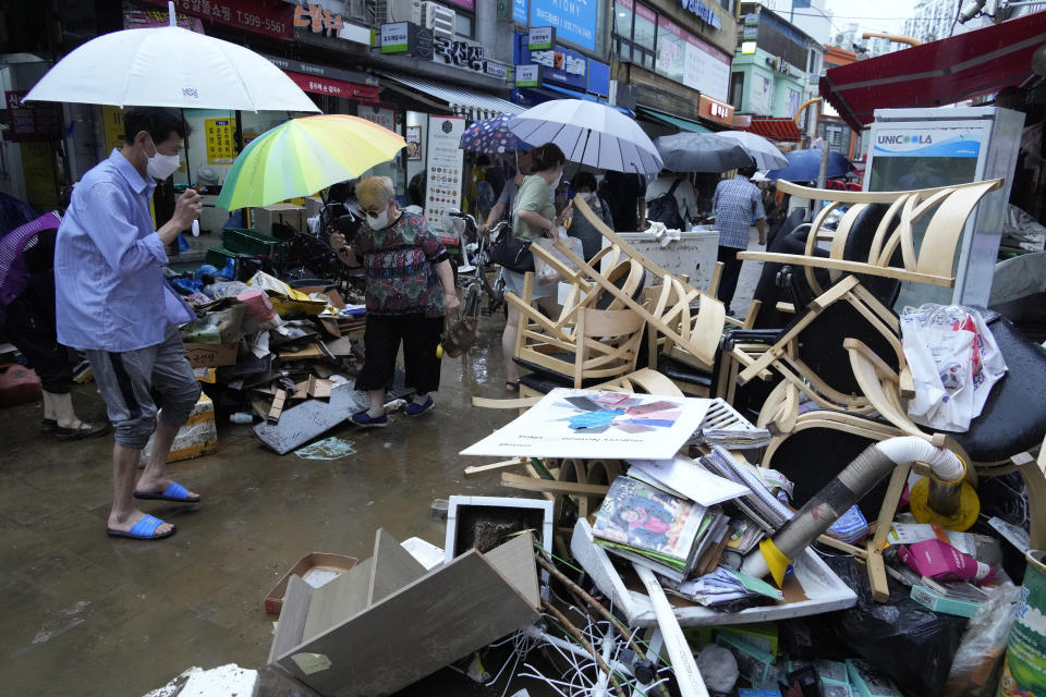 People pass by debris after the water drained from a submerged traditional market following heavy rainfall in Seoul, South Korea, Tuesday, Aug. 9, 2022. Heavy rains drenched South Korea's capital region, turning the streets of Seoul's affluent Gangnam district into a river, leaving submerged vehicles and overwhelming public transport systems. (AP Photo/Ahn Young-joon)