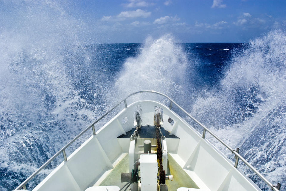 The bow of a ship ploughs through heavy seas and spray in open ocean.