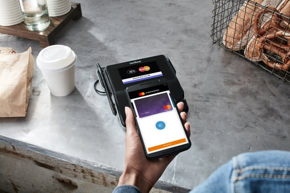 Customer holding smartphone, with it displaying Masterpass, using it to make a payment at a bakery.