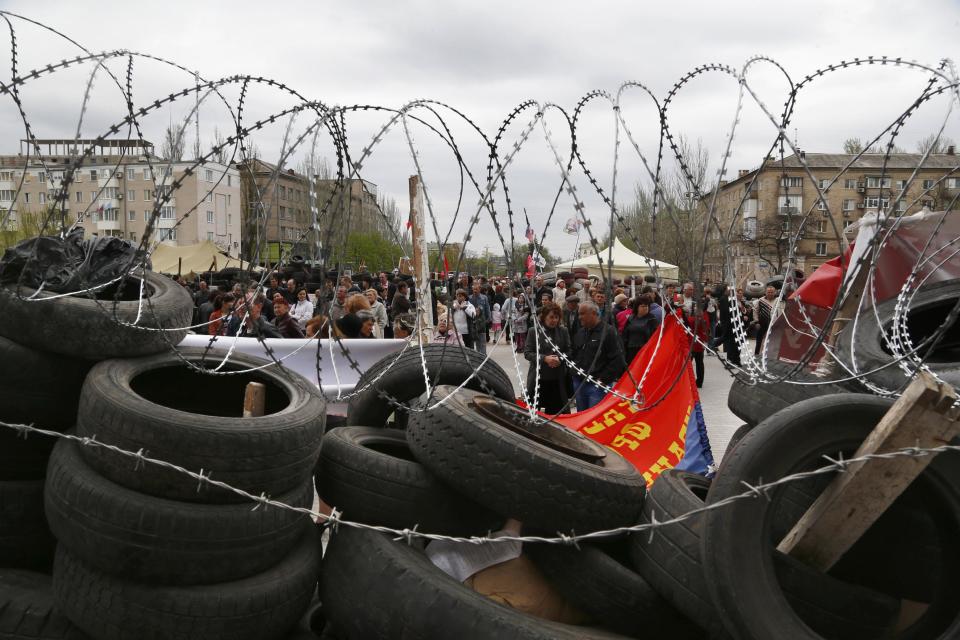 People stand at a barricade at the regional administration building that they had seized earlier in Donetsk, Ukraine, Sunday, April 20, 2014. The Ukrainian and Russian governments are reporting a shootout at a checkpoint set up by pro-Russian insurgents in eastern Ukraine that has left one person dead and others hospitalized with gunshot wounds. (AP Photo/Sergei Grits)