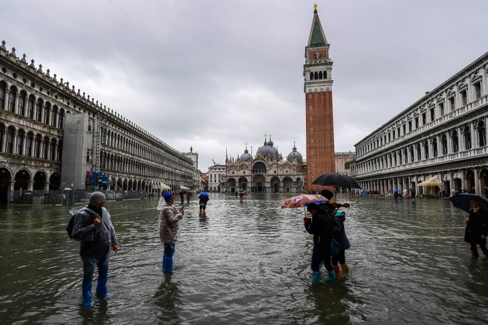 People walk across the flooded St. Mark's Square, by the Bell Tower (R) and St. Mark's Basilica (Rear) on November 24, 2019 in Venice during a high tide "Acqua Alta" meteorological phenomenon with a high of 140 cm expected. - Flood-hit Venice was bracing for another, though smaller, high tide on November 24, after Italy declared on November 15 a state of emergency for the UNESCO city where perilous deluges have caused millions of euros worth of damage. (Photo by Miguel MEDINA / AFP) (Photo by MIGUEL MEDINA/AFP via Getty Images)