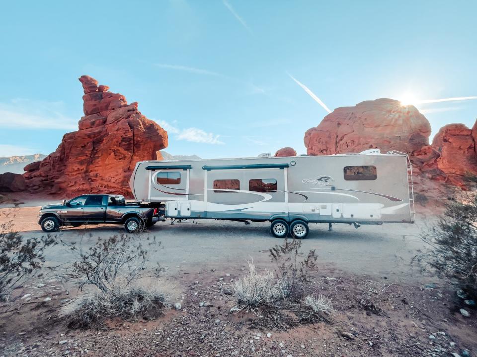 Truck pulling large home RV in front of red rock landscape