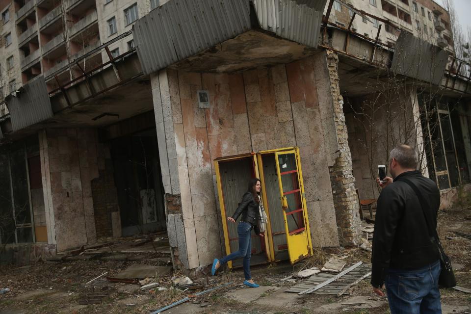 <p>Tourists on a guided tour snap photos of one another outside an abandoned shop and apartment building (Getty Images) </p>