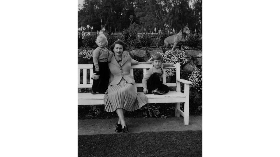 Queen Elizabeth sitting with her children, Charles and Anne and a royal corgi in the garden of Balmoral Castle in Scotland in 1952