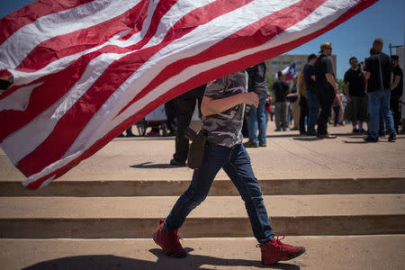 Christian Kaufman, 9, walks past an American flag while carrying a airsoft gun in a holster during an open carry firearm rally on the sidelines of the annual National Rifle Association (NRA) meeting in Dallas, Texas, U.S., May 5, 2018. REUTERS/Adrees Latif