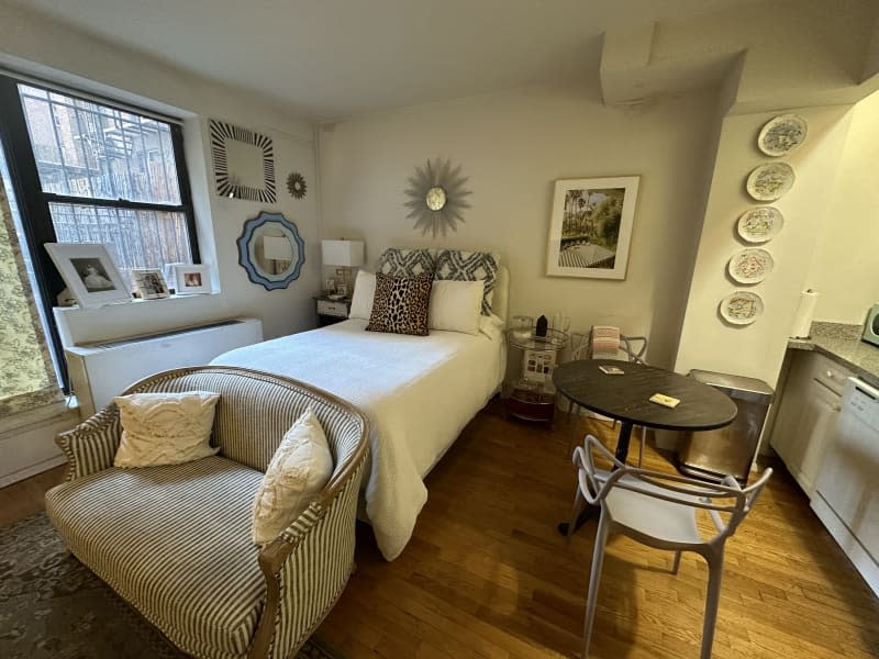 A decorated studio sleeping area with a lovely seat at the end of the bed.