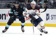 Edmonton Oilers center Connor McDavid (97) skates with the puck ahead of Seattle Kraken center Riley Sheahan (15) during the second period of an NHL hockey game Friday, Dec. 3, 2021, in Seattle. (AP Photo/Elaine Thompson)