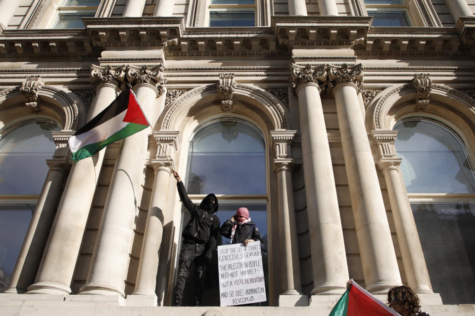 Demonstrators hold up flags and placards as they stand on the window ledge of government buildings in Whitehall during a pro Palestinian demonstration in London, Saturday, Oct. 21, 2023. (AP Photo/David Cliff)