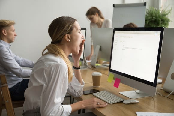 A woman yawns in front of her computer at work.