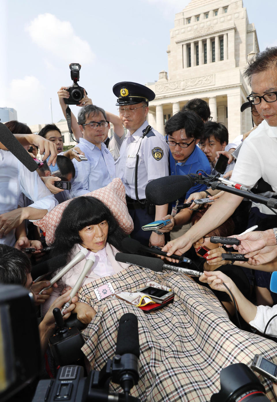 Newly-elected lawmaker Eiko Kimura in a wheelchair is surrounded by journalists as she arrives at the parliament building, background, to attend an extraordinary session of the upper house in Tokyo Thursday, Aug. 1, 2019. Japan’s parliament convened after elections and a minor renovation at the upper house. Kimura, who has cerebral palsy, won the July 21 elections, representing an opposition group. (Yohei Funai/Kyodo News via AP)