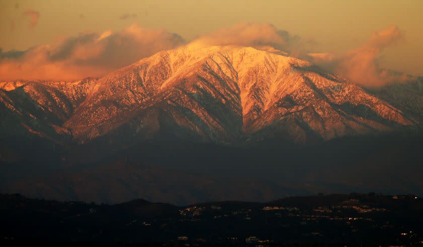 The setting sun casts a golden glow on the snow-covered peaks of Mt. Baldy.