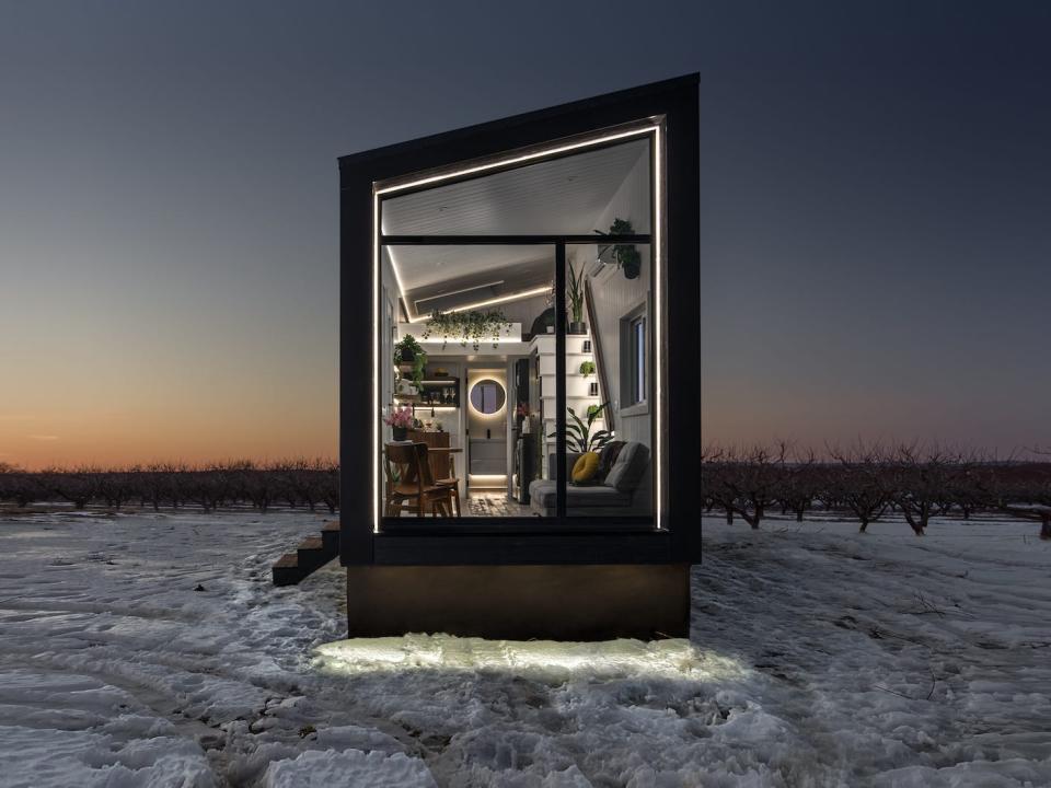 a black tiny home with a large glass wall on a snowy field