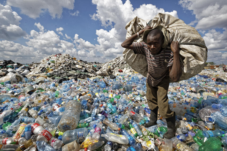 FILE - In this Wednesday, Dec. 5, 2018 file photo, a man walks on a mountain of plastic bottles as he carries a sack of them to be sold for recycling after weighing them at the dump in the Dandora slum of Nairobi, Kenya. The oil industry in 2020 has asked the United States to pressure Kenya to change its world-leading stance against the plastic waste that litters Africa, according to environmentalists who fear the continent will be used as a dumping ground. (AP Photo/Ben Curtis, File)