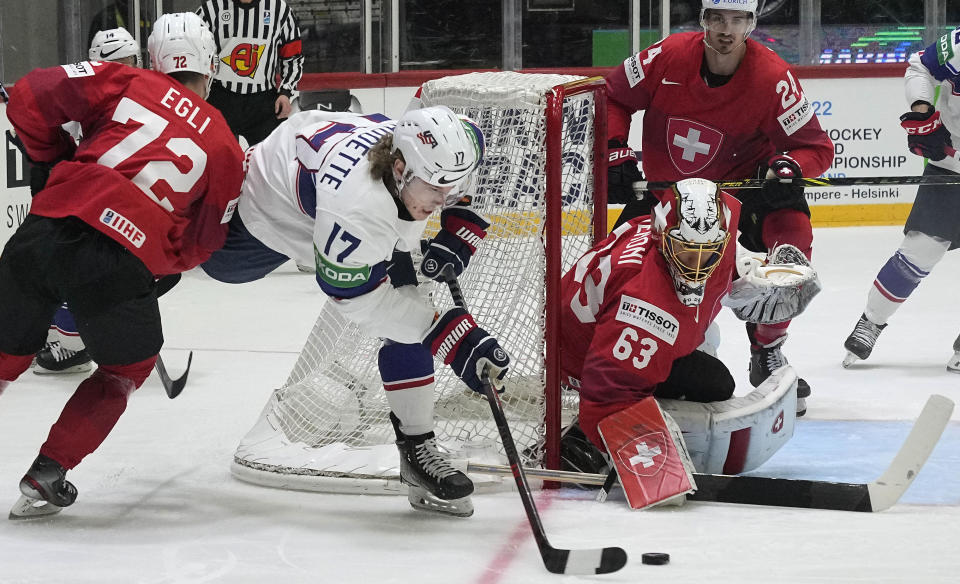 Adam Gaudette of the United States, center, challenges with Switzerland's Dominik Egli, left, and Switzerland's keeper Leonardo Genoni, right, during the Hockey World Championship quarterfinal match between Switzerland and USA in Helsinki, Finland, Thursday May 26, 2022. (AP Photo/Martin Meissner)