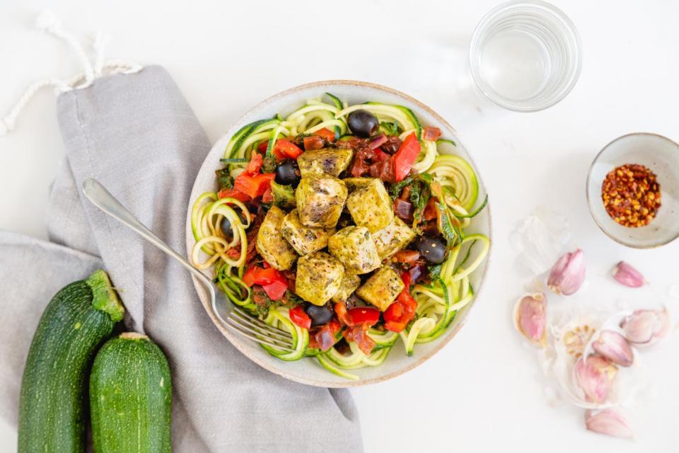 This vegan take on classic pasta might not get nonna’s approval but we challenge you to resist it.Cubed tofu fried in basil pesto, served with olive and sundried tomato ragu, on courgetti. We’ll call it fusion. Basil pesto tofu, courgetti and black olivesRecipe for two people, halve the ingredients for one person Macros: 483 calories • 27g carbs • 31g fat • 27g protein Allergens: Nuts, Soya Ingredients * 1/2 tsp red chilli flakes * 1 red onion * 1 red pepper * 1 tbsp oil * 200g passata * 2 tbsp vegan basil pesto * 2 tsp dried oregano * 2 tsp sunflower seeds * 300g courgette * 300g firm tofu * 30g Belazu naturally-ripened pitted black olives * 40g spinach * 60g sundried tomatoes Method1. Dice the onion and the red pepper. Slice the black olives and sundried tomatoes in half. Rinse the tofu and cut the tofu into small 1-2cm cubes. Pat dry with paper towel.2\. Heat a frying pan with 1 tsp oil on a medium heat and cook the tofu for 10 mins until turning golden. Stir in the basil pesto and season with a pinch of sea salt and black pepper, cook for 5 mins.3. Meanwhile, heat a medium-sized pan with 1 tsp oil on a medium heat and cook the red onion for 5 mins, then add the red pepper for 3 mins. Stir in the passata, spinach, sundried tomatoes, black olives, dried oregano and a pinch of red chilli flakes (as many as desired). Simmer for 5 mins until thickened. Season with a pinch of sea salt and black pepper.4\. Meanwhile, to make the courgetti noodles; remove the ends of the courgettes, but leave the skin on. Prepare the courgette noodles using a peeler and slice the courgettes into long thin strips (or use a julienne peeler or spiralizer if you have one).5\. Remove the tofu from the pan, cover and keep warm. Heat the same frying pan with 1 tsp oil on a medium heat and cook the courgetti for 1 minute until softened.6\. Spoon the courgetti into two warm bowls, top with the tomato sauce then the basil pesto tofu. Sprinkle with the sunflower seeds.For more recipe ideas follow Mindful Chef on Instagram at @mindfulchefuk and check out the website.