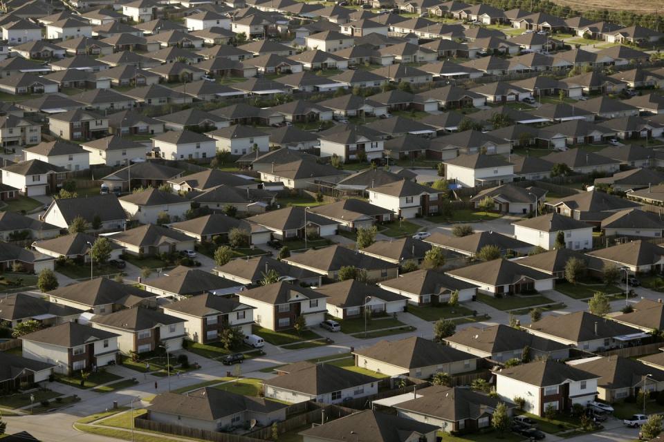 An aerial view shows suburban houses, all similar with dark roofs and white exteriors.