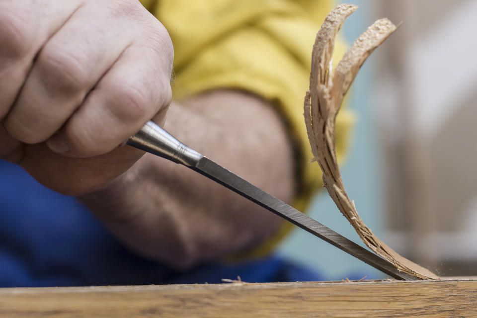 Carpenter makes a hole in old wooden door for the mortise lock with a hammer and chisel. Close-up.