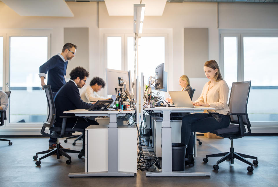 People working on laptop at their desk with manager supervising the work. Business people working in a small office.