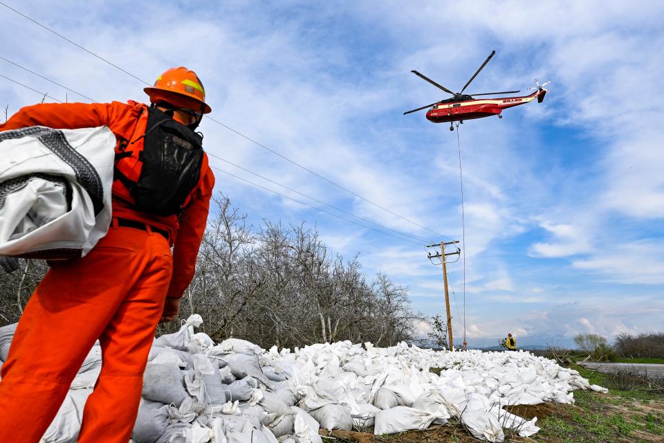 A member of an inmate hand crew watches a helicopter place a large bag of gravel Friday, March 17, 2023 along a break in the Tule River east of Road 192 just north of Avenue 168 and east of Woodville. Road closures are common in south Tulare County. Flood warnings have been issued for many areas.