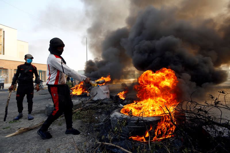 FILE PHOTO: Protester pours fuel on a tire to burn it as he blocks a street during ongoing anti-government protests in Najaf