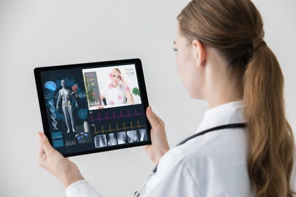 A female doctor holding a tablet and having a virtual consultation with a female patient