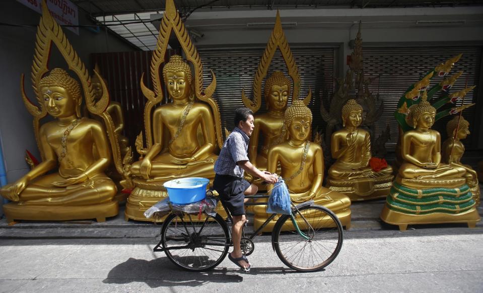 In this Thursday, Jan. 12, 2017 photo, a cyclist passes a row of Buddha statues in Bangkok, Thailand. Buddhism is the predominant religion in the country. (AP Photo/Sakchai Lalit, File)