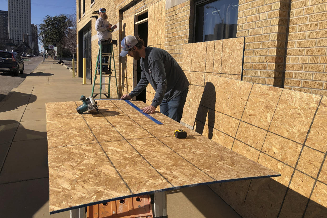 Ryan Kellum, center, and Ricky Noe install plywood boards over windows at Caliber Collision, Friday, Jan. 27, 2023, in Memphis, Tenn. Kellum said the company he works for was putting up boards over windows at the downtown Memphis business ahead of the release of the video of Tyre Nichols' arrest. (AP Photo/Adrian Sainz)