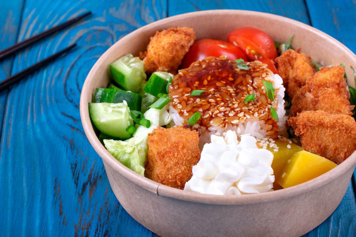 Poke bowl with fried chicken, vegetables and rice on the blue wooden table. Hawaiian cuisine meal