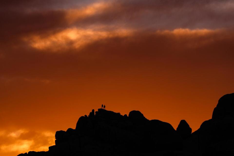 Hikers take in a sunset on top of rocks in Joshua Tree National Park in Jan. 2022.
