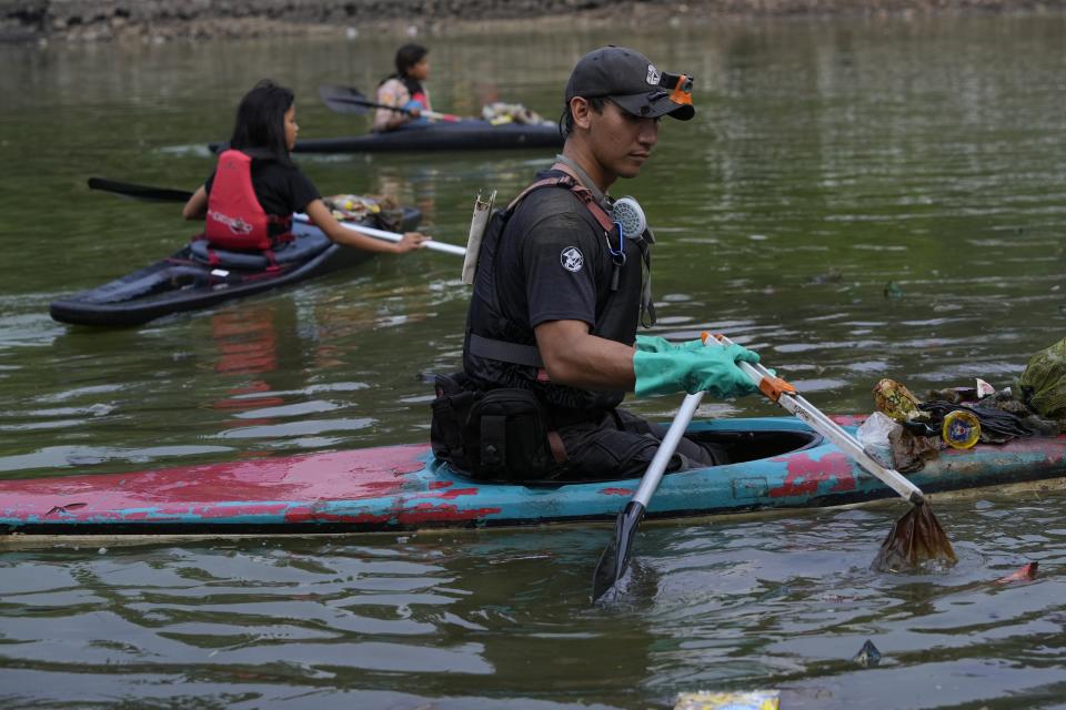 Environmental activist Giri Marhara picks up trash while paddling a kayak at Setu Gede lake in Bogor, West Java, Indonesia, Tuesday, Oct. 10, 2023. Young people like Marhara have been at the forefront of environmental and climate change movements in recent years: initiatives like school strikes for climate action, protests at United Nations climate talks and around the world, and local clean ups have often been youth-led. (AP Photo/Achmad Ibrahim)