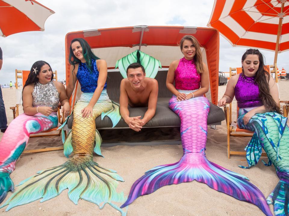 cast of merpeople in mermail tails on a beach