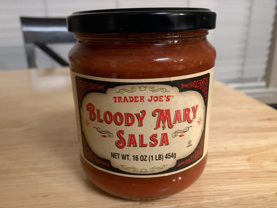 Trader joe's bloody mary salsa in its original glass jar on a light wood table