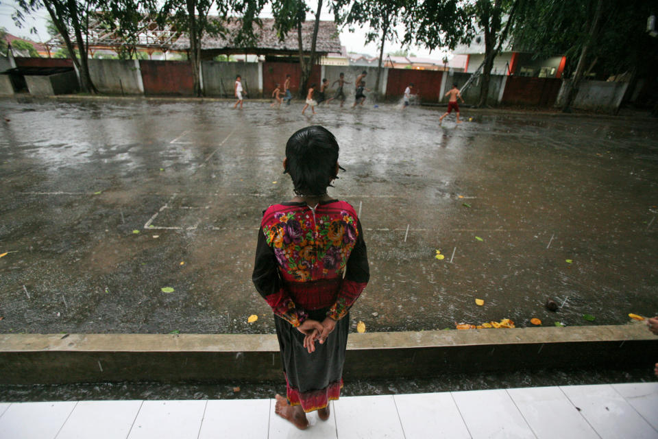 In this Aug. 7, 2013 photo, Senwara Begum, a young ethnic Rohingya asylum seeker, watches her friends play in the rain outside their temporary shelter in Medan, North Sumatra, Indonesia. After her tiny Muslim village in Myanmar's northwest Rakhine had been destroyed in a fire set by an angry Buddhist mob, she and her brother became separated from their family. (AP Photo/Binsar Bakkara)