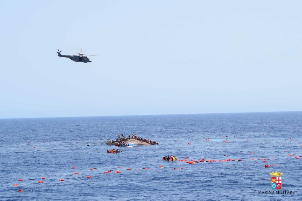 SICILIAN STRAIT, MEDITERRANEAN SEA - MAY 25: A helicopter approaches to the capsized boat as Italian marines rescue migrants from an overcrowded boat at Sicilian Strait, between Libya and Italy, in Mediterranean sea on May 25, 2016. The Italian Navy saved around 500 migrants as they found dead bodies of seven migrants in the sea during the operations. (Photo by Italian Navy / Marina Militare/Anadolu Agency/Getty Images)