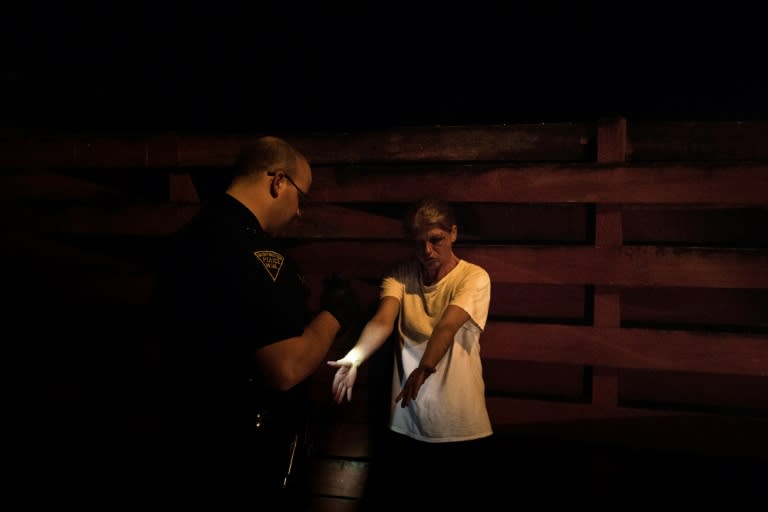 A woman suspected of acting under the influence of heroine shows her arms to a Huntington police officer in Huntington, West Virginia