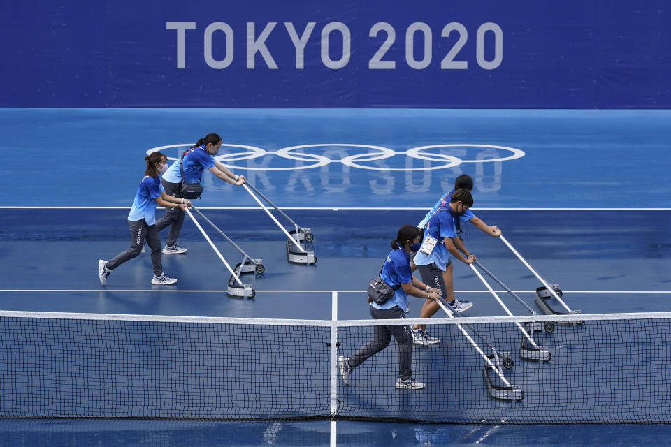 Workers push water off of a court during a rain delay in the tennis competition at the 2020 Summer Olympics, Tuesday, July 27, 2021, in Tokyo, Japan. (AP Photo/Patrick Semansky)