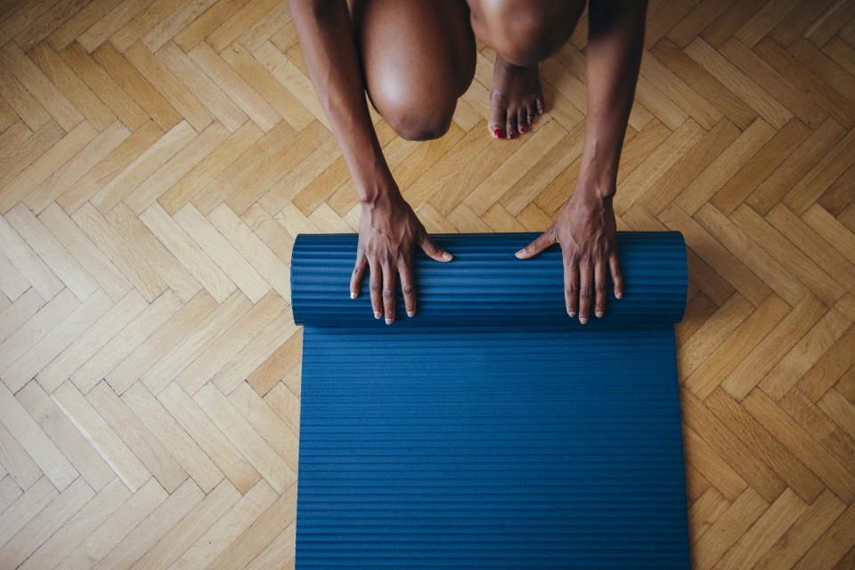 From above photo of unrecognizable African-American woman folding fitness mat before or after working out at home