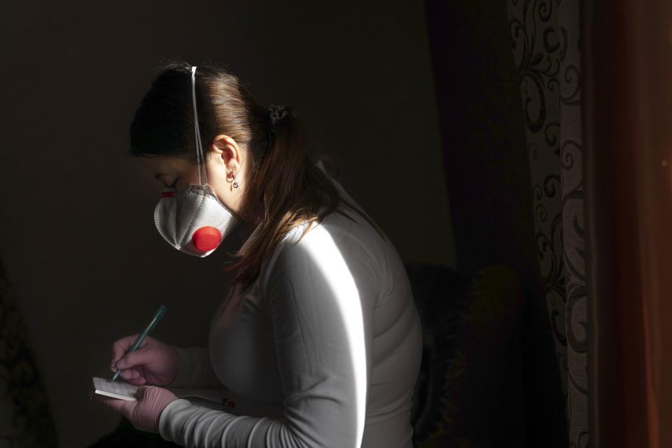 Dr. Viktoria Mahnych, wearing face mask against coronavirus, writes down a note as she visits a patient with COVID-19 in Verhovyna village, Ivano-Frankivsk region of Western Ukraine, Wednesday, Jan. 6, 2021. Mahnych fears that a lockdown in Ukraine came too late and the long holidays, during which Ukrainians frequented entertainment venues, attended festive parties and crowded church services, will trigger a surge in new coronavirus infections. (AP Photo/Evgeniy Maloletka)