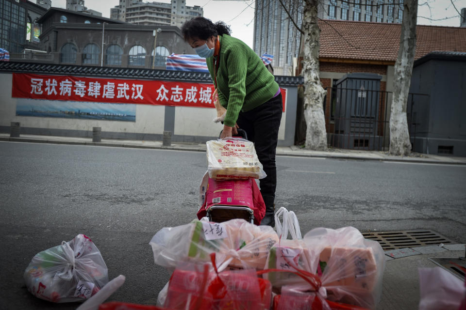 In this Saturday, Feb. 22, 2020, photo, a woman using a trolley bag to collect foods distributed by volunteers outside her home in Wuhan in central China's Hubei province. South Korea and China both reported a rise in new virus cases on Sunday, as the South Korean prime minister warned that the fast-spreading outbreak linked to a local church and a hospital in the country's southeast had entered a "more grave stage." (Chinatopix via AP)