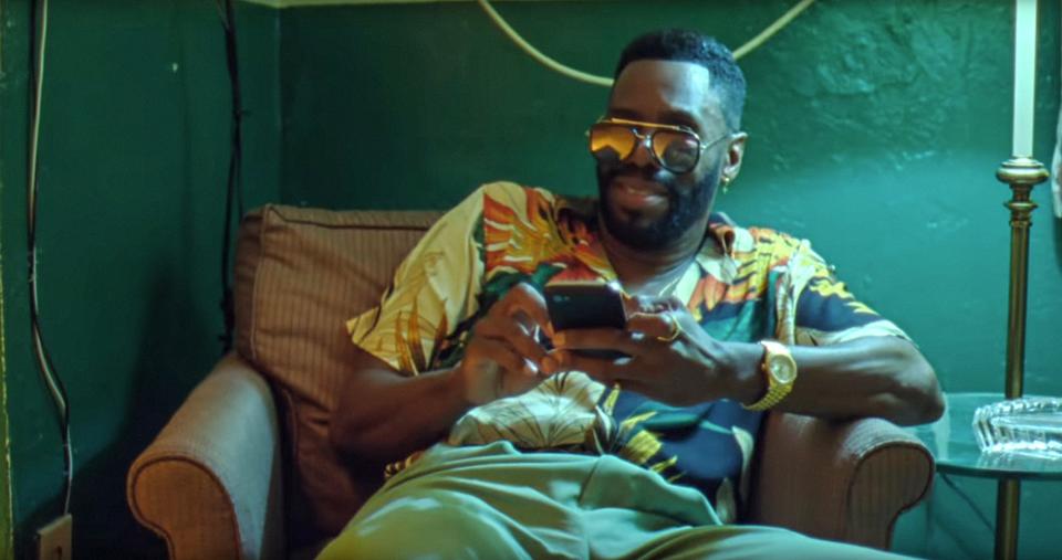 a man in a dark room siting on a couch wearing sunglasses and on his phone