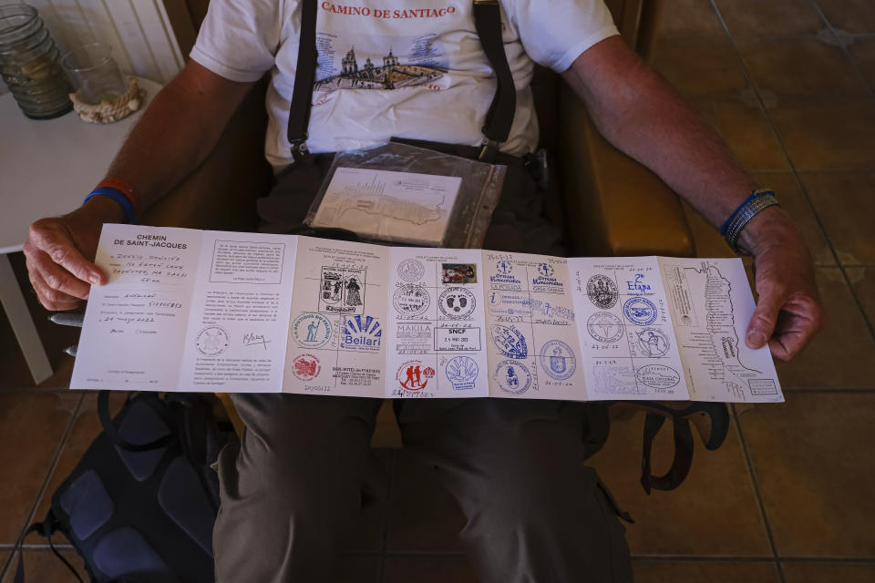 Dennis Dowling, 75, from United States, shows his Saint James' passport during a stage of "Camino de Santiago" or St. James Way in Uterga, northern Spain, Sunday, May 29, 2022. Over centuries, villages with magnificent artwork were built along the Camino de Santiago, a 500-mile pilgrimage route crossing Spain. Today, Camino travelers are saving those towns from disappearing, rescuing the economy and vitality of hamlets that were steadily losing jobs and population. “The Camino is life,” say villagers along the route. (AP Photo/Alvaro Barrientos)