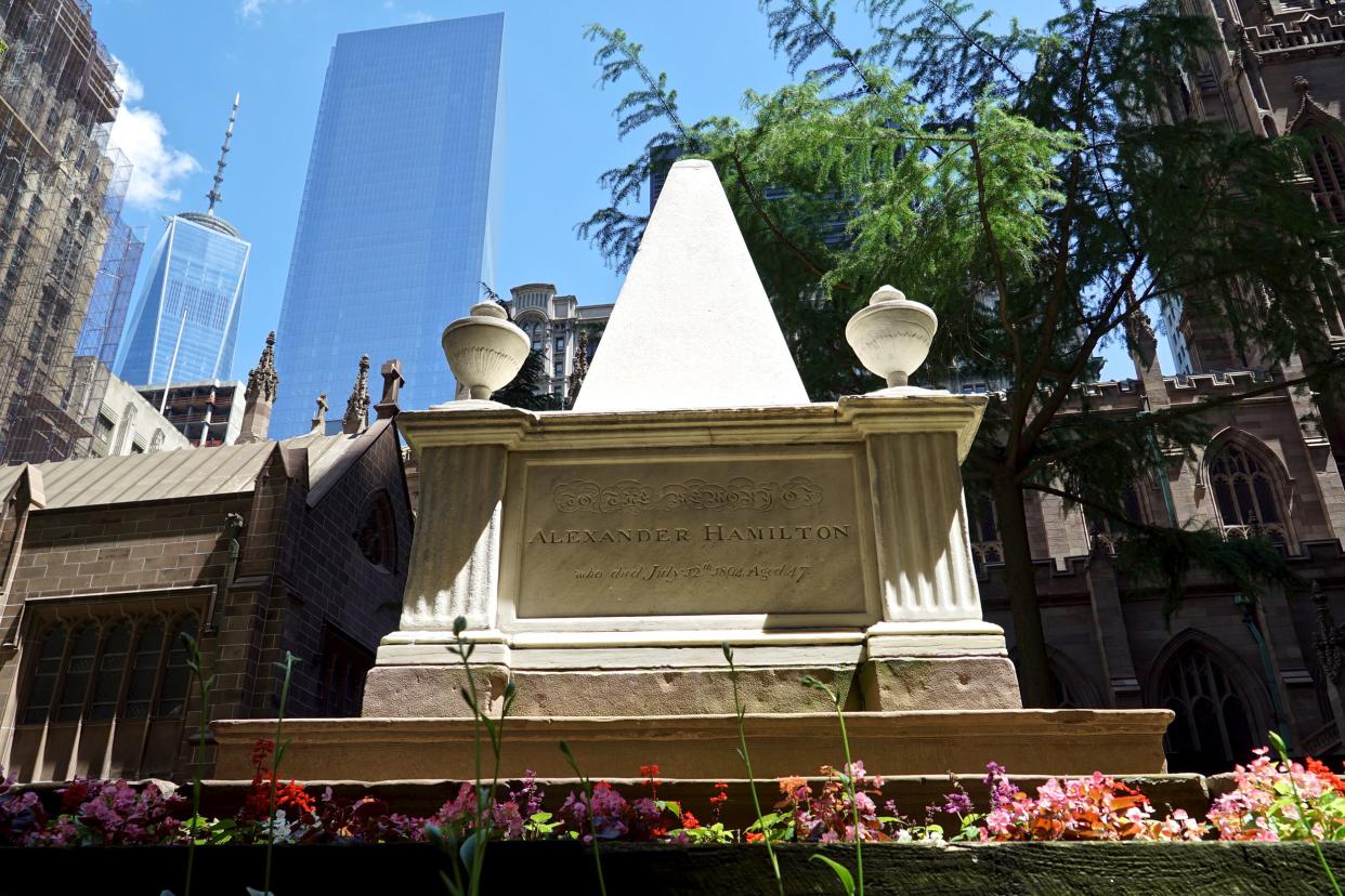 Alexander Hamilton's tomb in the Trinity Churchyard, New York City with a row of flowers in the foreground on a bright summer day with the One World Trade Center and other buildings in the background