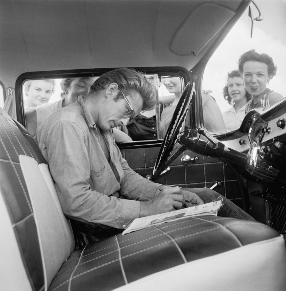 <p>Dean's car is stopped by fans for autographs while filming <em>Giant. </em>This was the third of Dean's major pictures, although at this time, only <em>East of Eden </em>had been released. </p>