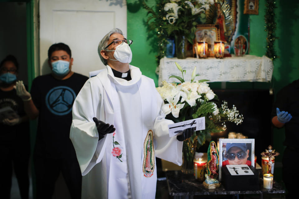 The Rev. Fabian Arias performs an in-home service beside the remains of Raul Luis Lopez who died from COVID-19 the previous month, Saturday, May 9, 2020, in the Corona neighborhood of the Queens borough of New York. (AP Photo/John Minchillo)