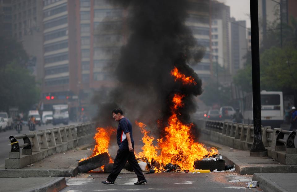 A pedestrian walks in front of a burning barricade blocking the highway in Chacao, Caracas, Venezuela, Monday, Feb. 24, 2014. Traffic has come to a halt in parts of the Venezuelan capital because of barricades set up by opposition protesters across major thoroughfares. The protests are part of a wave of anti-government demonstrations that have swept Venezuela since Feb. 12 and have resulted in at least 10 deaths. The protests in the capital Monday were peaceful. Police and National Guard troops stood by but did not act to remove the barricades despite the effect on the morning commute. (AP Photo/Rodrigo Abd)