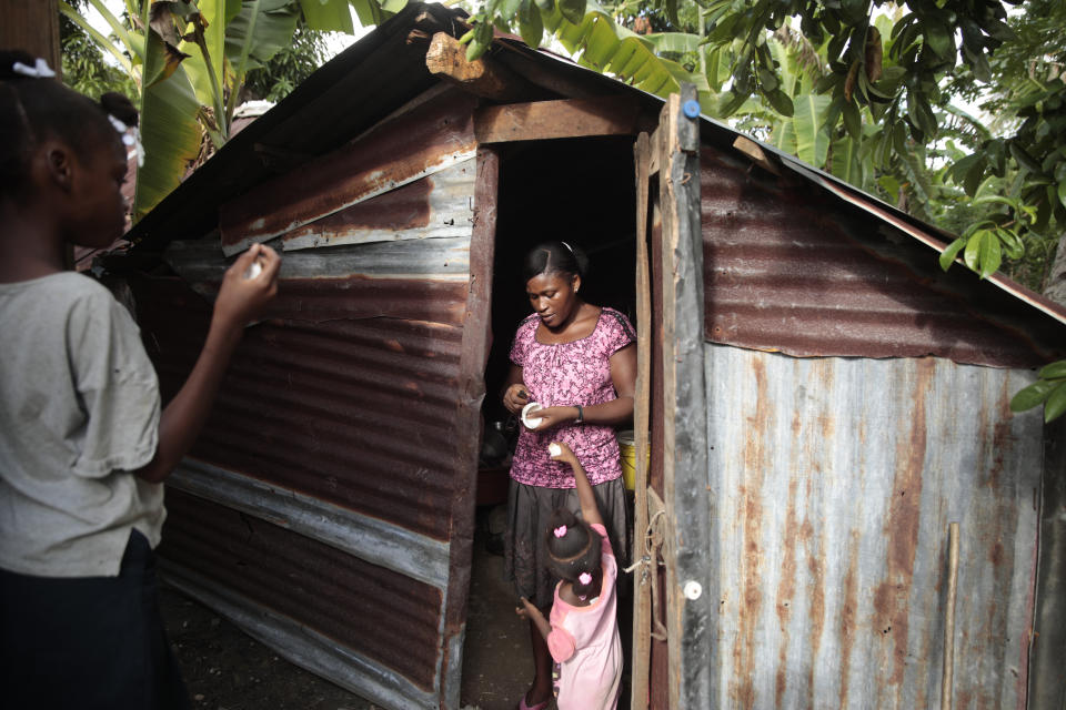 Renèse Estève corta trozos de coco para sus hijas Manouchi Victor, abajo, y Routcheland Veillard, en su casa en una zona rural de Saint-Louis-du-Sud, Haití, el jueves 25 de mayo de 2023. Otros dos hijos de Estève estuvieron considerados como "huérfanos de pobreza" durante tres años después de que los dejara en un orfanato creyendo que estarían mejor atendidos. Su madre se los llevó a casa tras asustarse por el peso que habían perdido, convencida de que estarían mejor en la pobreza extrema. (AP Foto/Odelyn Joseph)