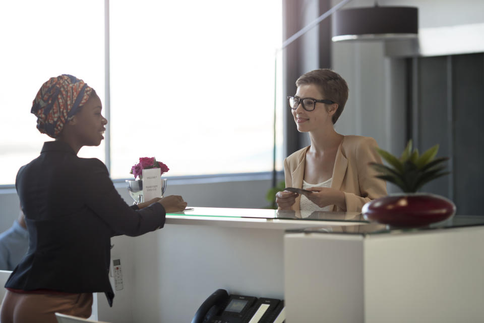 Two people at a hotel reception, one employee handing a key card to the other, suggesting a travel-related service interaction