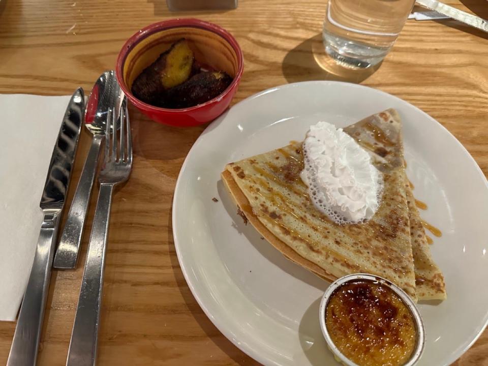 Plate with a crepe and whipped cream on top with a small creme brulee on the plate next to silverware