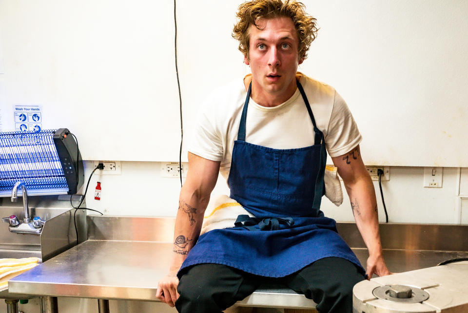 Carmy looking frazzled and sitting on a prep table in the kitchen in a scene from "The Bear"