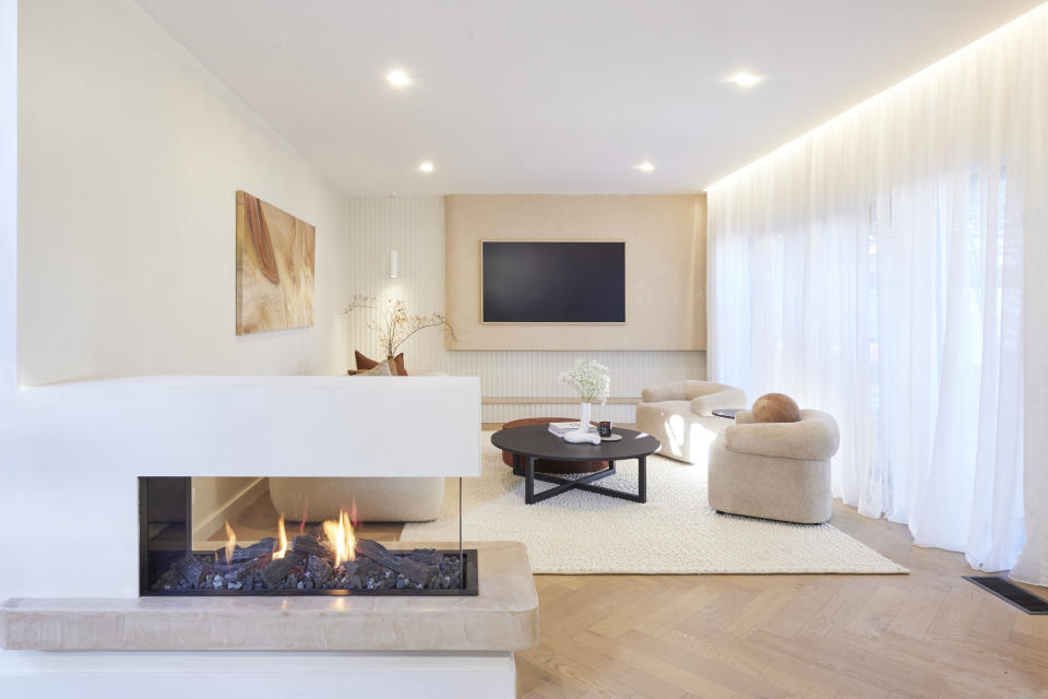 A wide shot of the living room, with the fireplace front left, a tv on the back wall and seating in the middle.